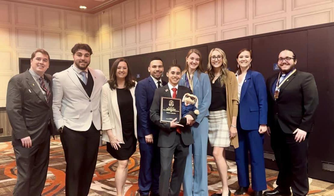 The speech and debate team is shown in formal wear holding their bronze award.